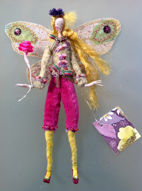GRETCHEN; A 16 cm fairy with a hand painted silk face - she is wearing a hand embroidered and beaded felt jacket and silk velvet breeches. She is holding a satin ribbon rose and has stiffly embroidered wings ( transparent in the light ) and a purple sequinned hat. She comes in an organza bag with a hand painted name tag. £35 plus £2 postage