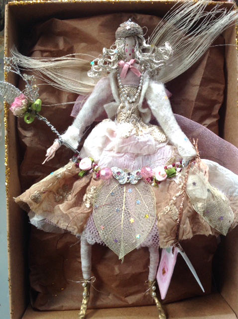 WINTER ROSE A 20cm high fairy with a painted silk head. She is wearing her best party dress , embellished with satin roses, beads, braid , a diamente butterfly and skeleton leaves. Over this is a silk felted jacket. She has white peacock feather wings , an acorn hat and is holding a dried rosebud wand. She comes in a Betty Bib box with a hand painted name tag. £50 plus £3.50 p&p.
