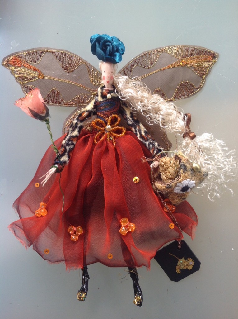 GALA, a 17cm high fairy with a silk painted head. This fairy is wearing a leopard skin long sleeved bolero over a paisley top and she has a chiffon and net skirt. She has a beaded flower at her waist , stiffly embroidered wings and is holding a wooden bag with a glittered alder cone inside it. She also has a fabric rose wand and a satin rose hat and a dried flower name tag. She comes in an organza bag with dried flowers in it. £40 plus P&P.