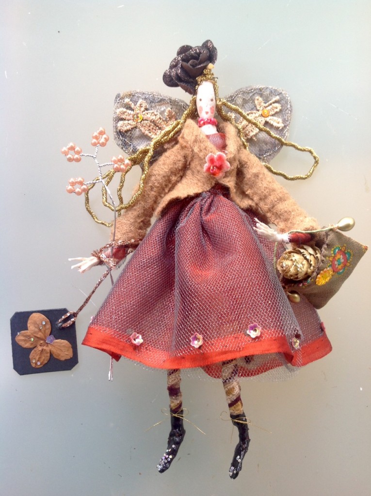 GIGI, a 17cm high fairy with a silk painted head and wearing a chiffon and fine tulle dress. She has patterned tights and patent boots. Her winter jacket is fine felted wool and has a velvet flower button. She has stiffly embroidered wings and she is holding a silk bag with a glittered alder cone inside it . She is also holding a pearl wand and a dried flower name tag. Her hat is a fabric rose. Gigi comes in an organza bag with dried flowers. £40 plus £3.50 p&p.