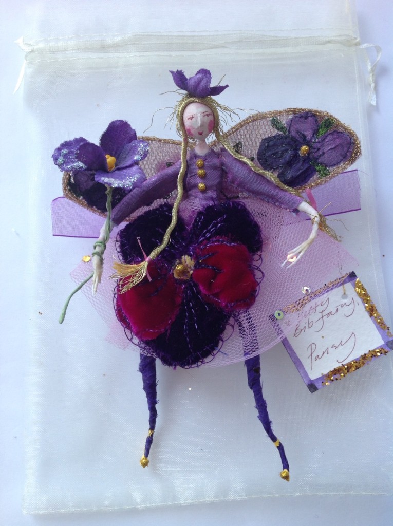 A 13cm high fairy with a clay painted head . She is wearing a velvet pansy embroidered skirt with a silk top. Her wings are stiffly embroidered with violas and she is holding a vintage violet and has an organza bow at her back. She comes in an organza bag with dried flowers. £38 plus £3.50 postage.